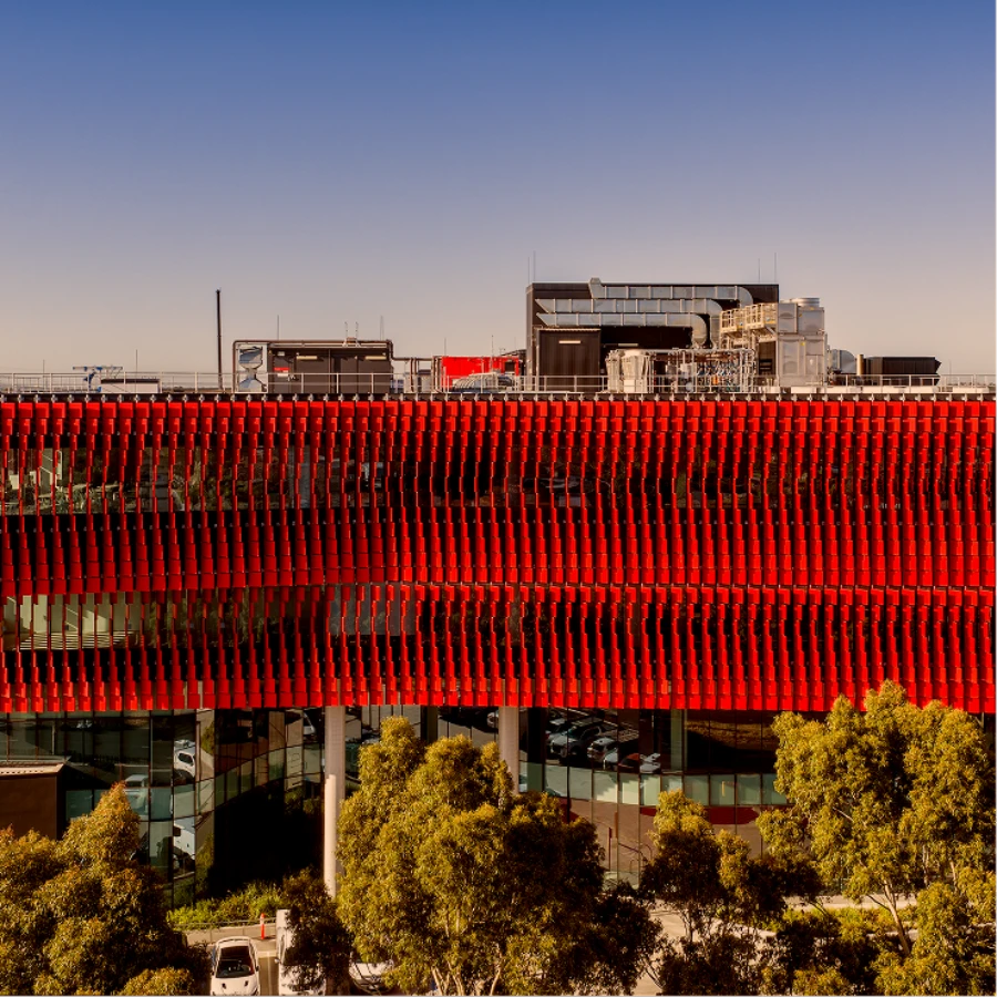 Building facade with an undulating red perforated metal louvre screen