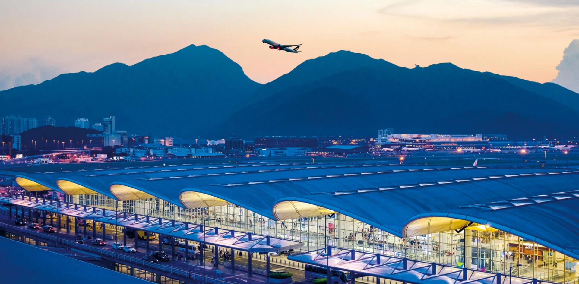 Hong Kong International Airport terminal at dusk with a departing aircraft