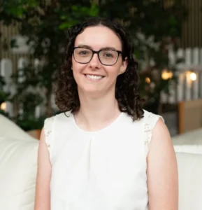 Headshot portrait of Lauren Malysiak smiling in front of greenery