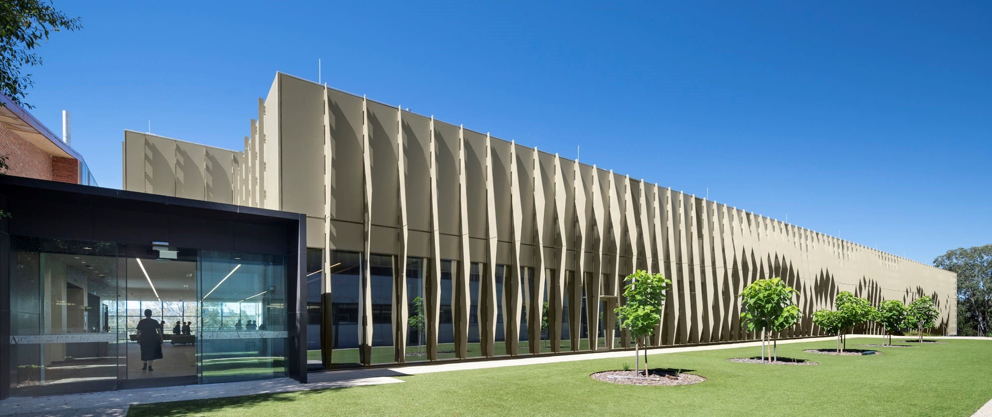 Building with a curved perforated bronze fin facade under a blue sky