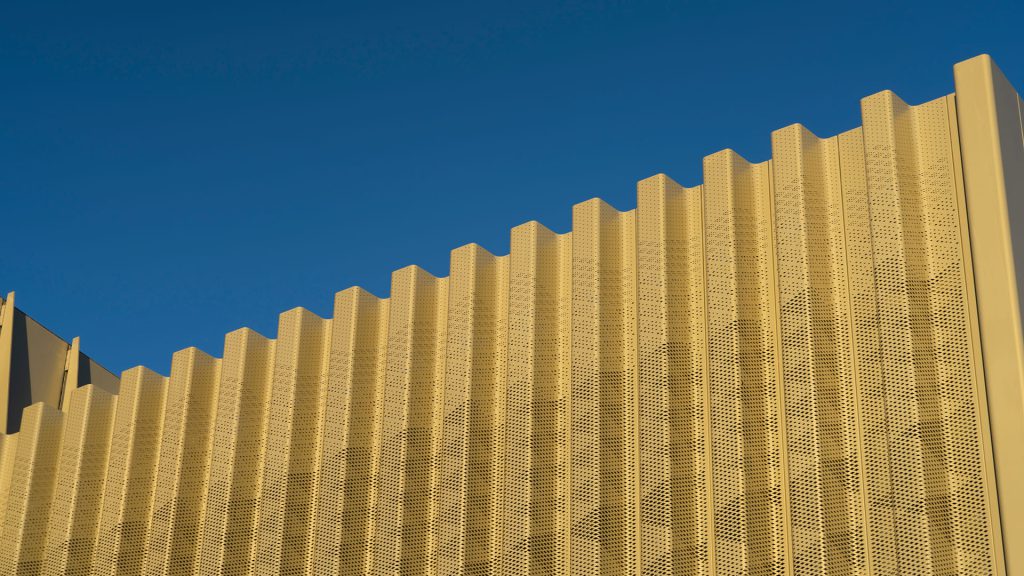 Close-up of a golden perforated metal fin facade against a blue sky