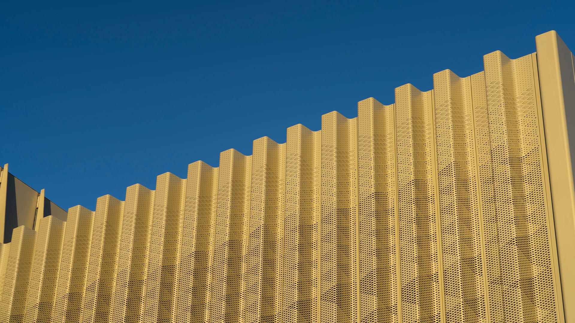 Close-up of a golden perforated metal fin facade against a blue sky