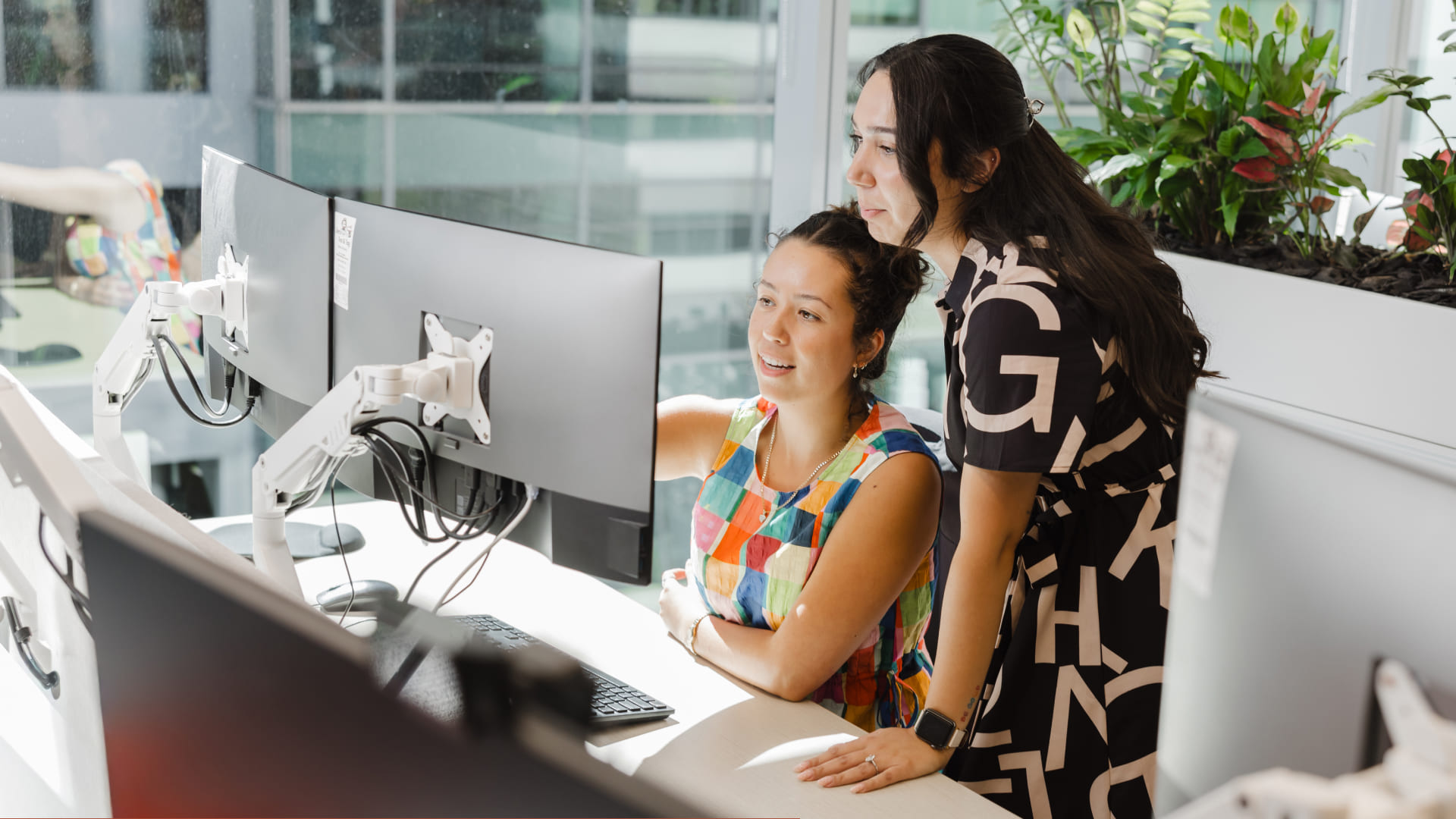 Two TTW colleagues reviewing work on dual monitors in a bright office