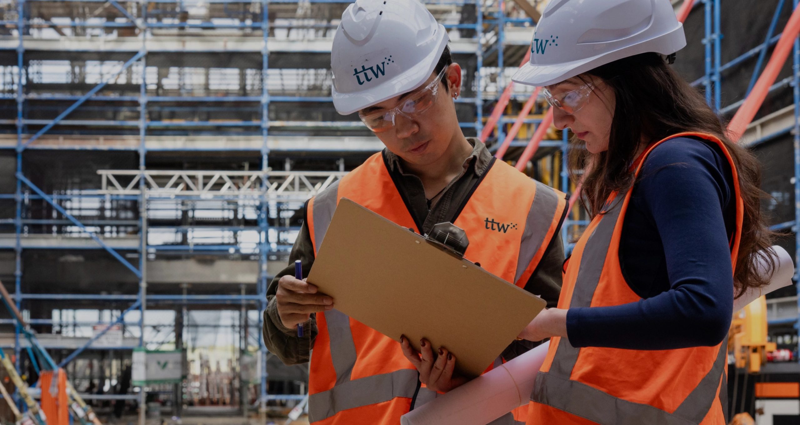 Two TTW engineers in hi-vis and hard hats reviewing a clipboard on a construction site