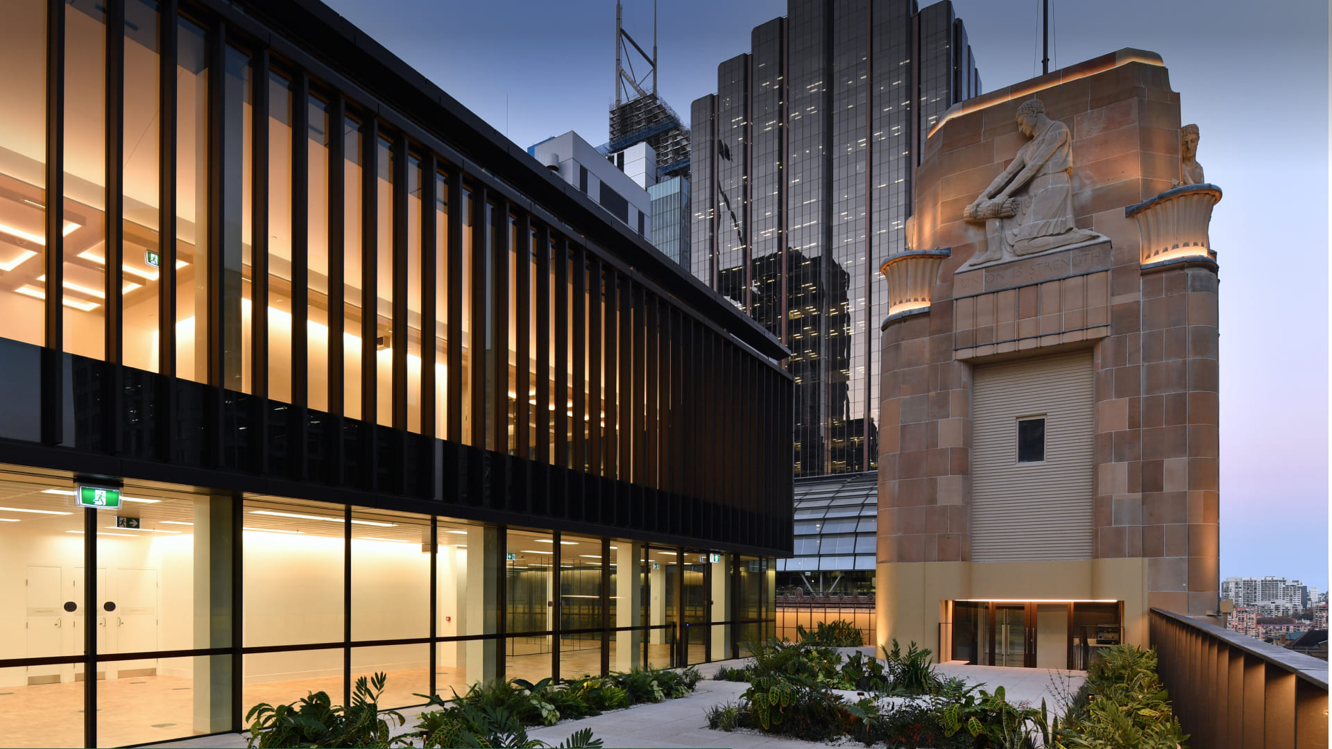 Rooftop terrace at dusk with a modern glass wing beside a heritage sandstone tower