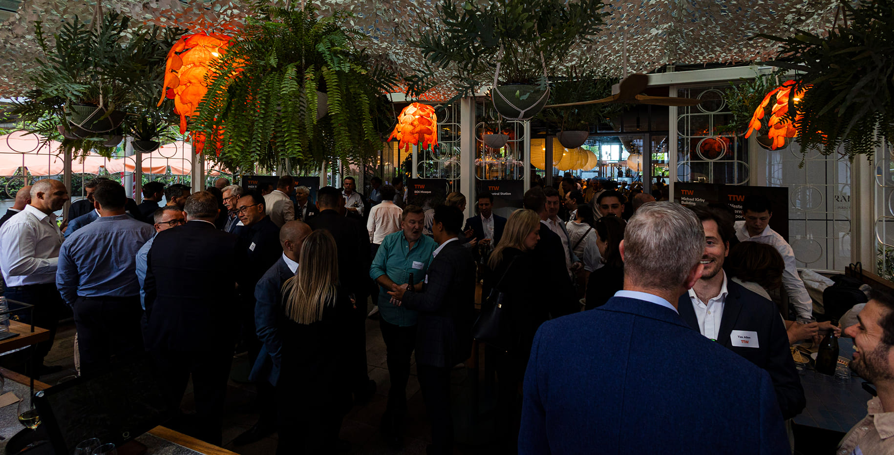 Guests networking at a TTW corporate event under hanging ferns and pendant lights