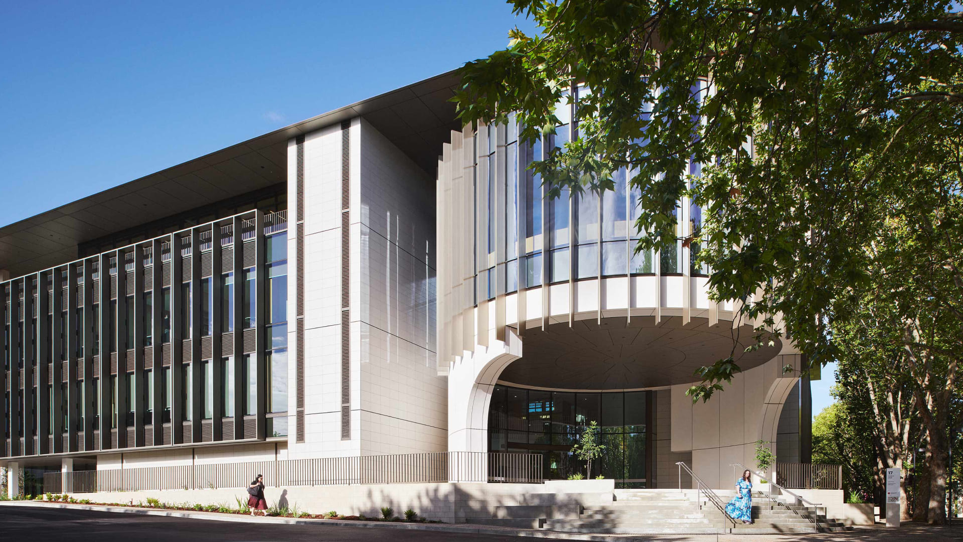 Modern institutional building with a curved glass fin facade and street trees