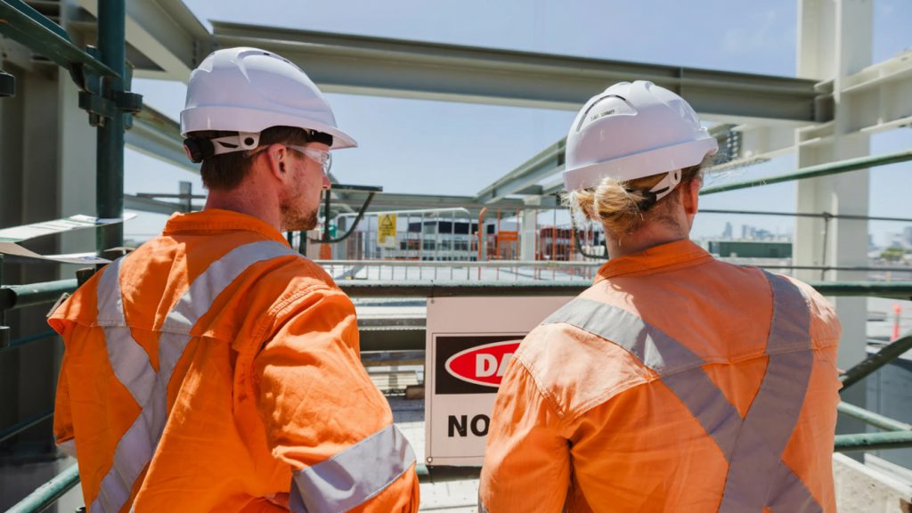 Two workers in orange hi-vis viewing a construction site from an elevated platform